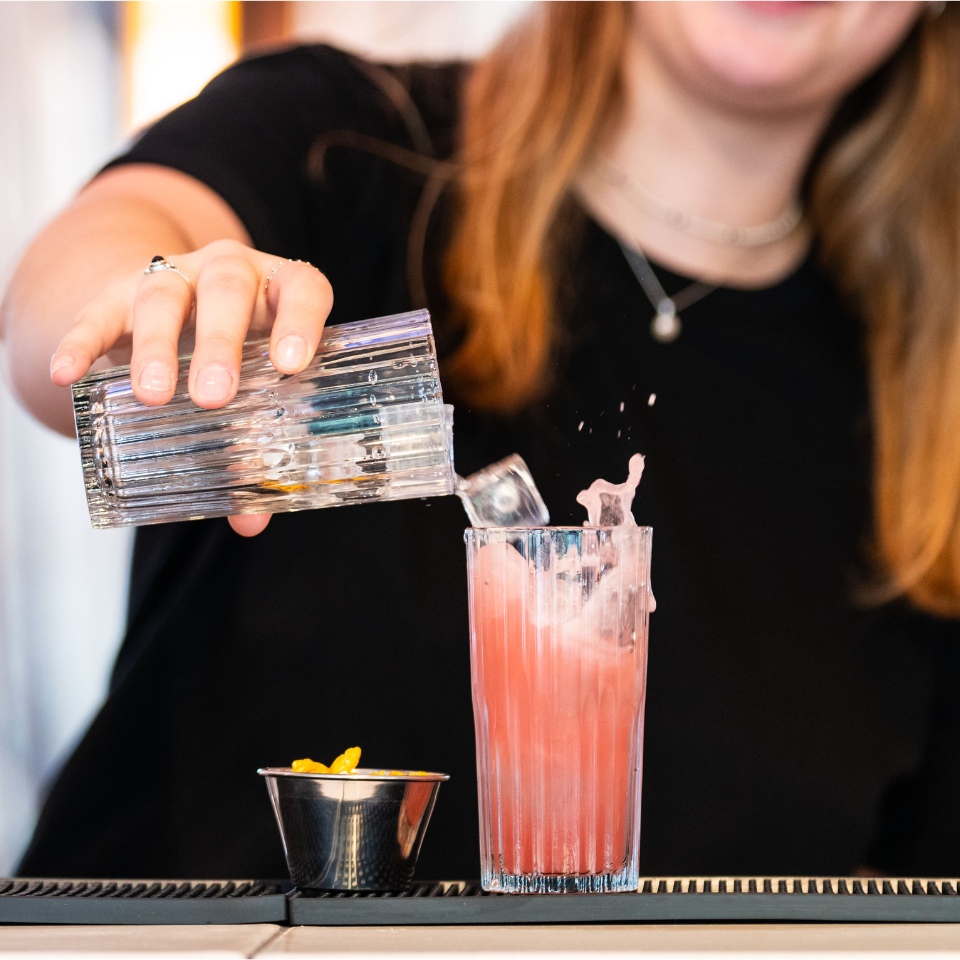 A bartender pouring a drink into a pink cocktail.