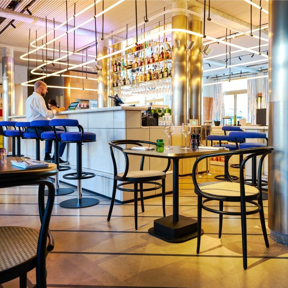 Bar and restaurant tables beside blue stools and large windows.