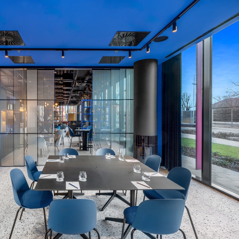 Salle de réunion avec un plafond bleu, des tables épurées et de grandes fenêtres donnant sur l’extérieur.