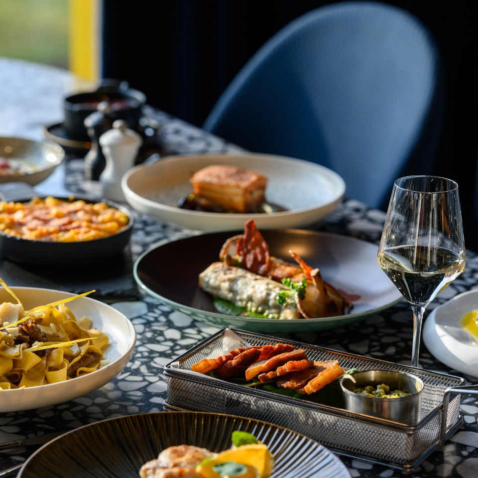 Une table joliment dressée avec de délicieux plats, dont des pâtes, des roulés salés et un verre de vin blanc.