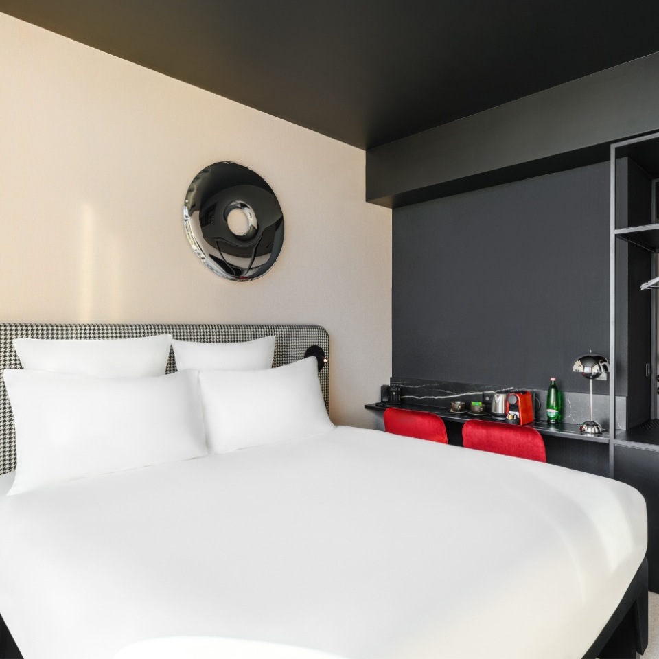 Chambre d’hôtel avec un grand lit blanc, des touches élégantes de noir et de rouge et un petit coin kitchenette.