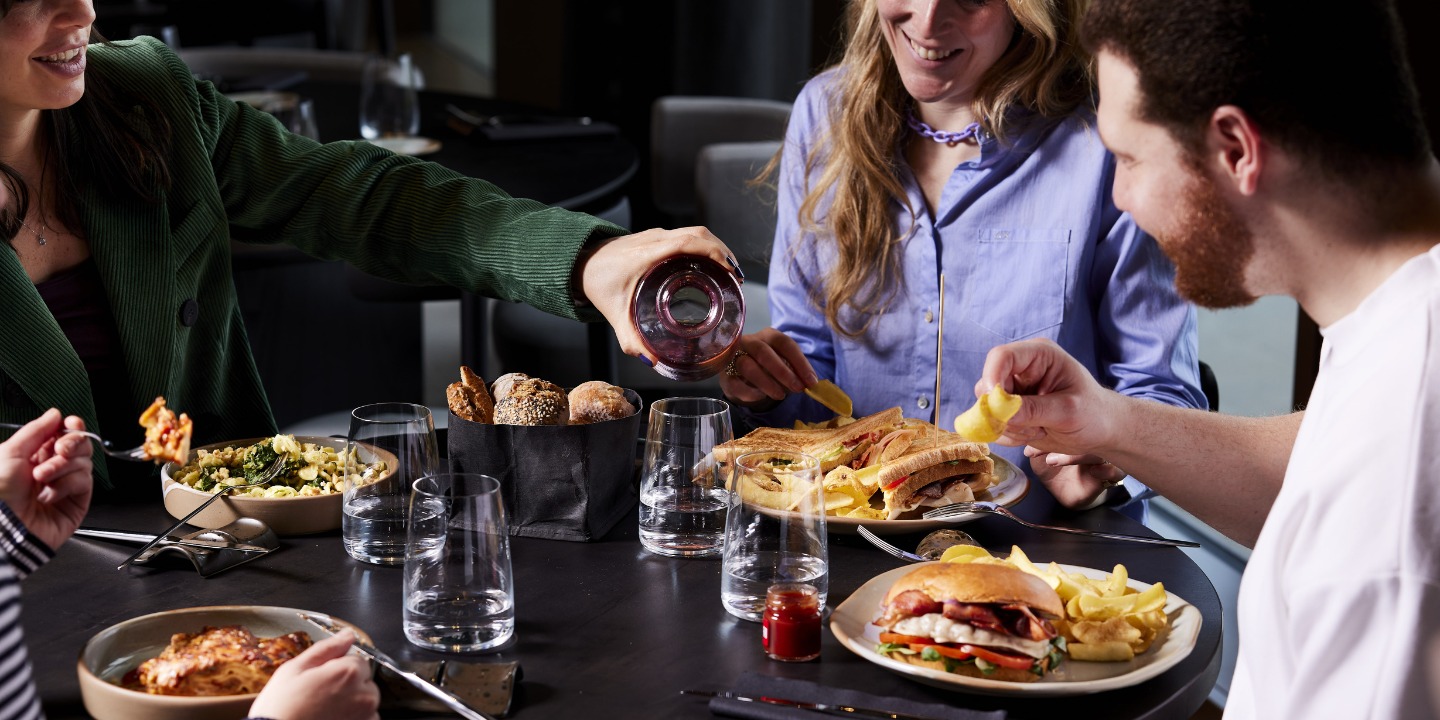A table is set with an assortment of food, including burgers, fries, and salad, alongside drinks and fresh breadrolls.