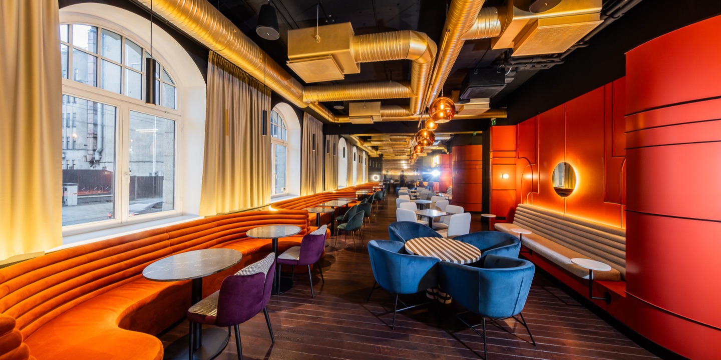 Stylish modern restaurant interior featuring curved orange booths, colorful chairs, and warm lighting along a wooden floor.