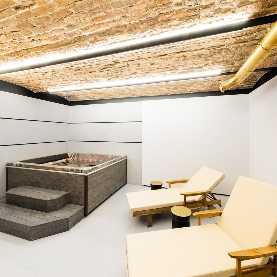 A serene spa room featuring a wooden hot tub, two lounge chairs, and a brick ceiling with modern LED lighting.
