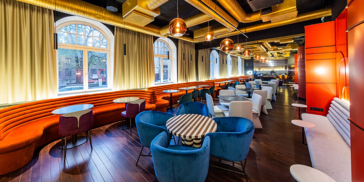 Stylish modern restaurant interior featuring curved orange booths, colorful chairs, and warm lighting along a wooden floor.