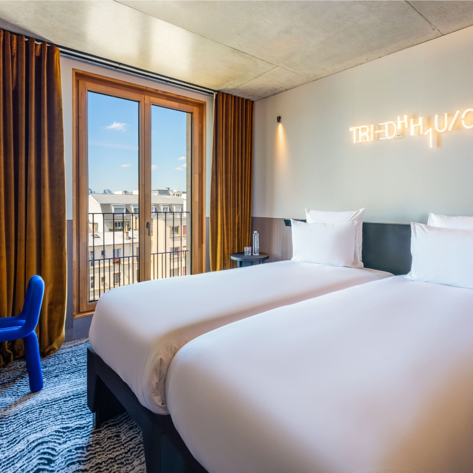 Twin beds beside a large window in a guest room.