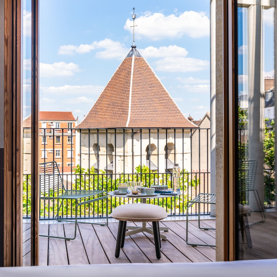 Table et chaises sur un balcon donnant sur les toits.
