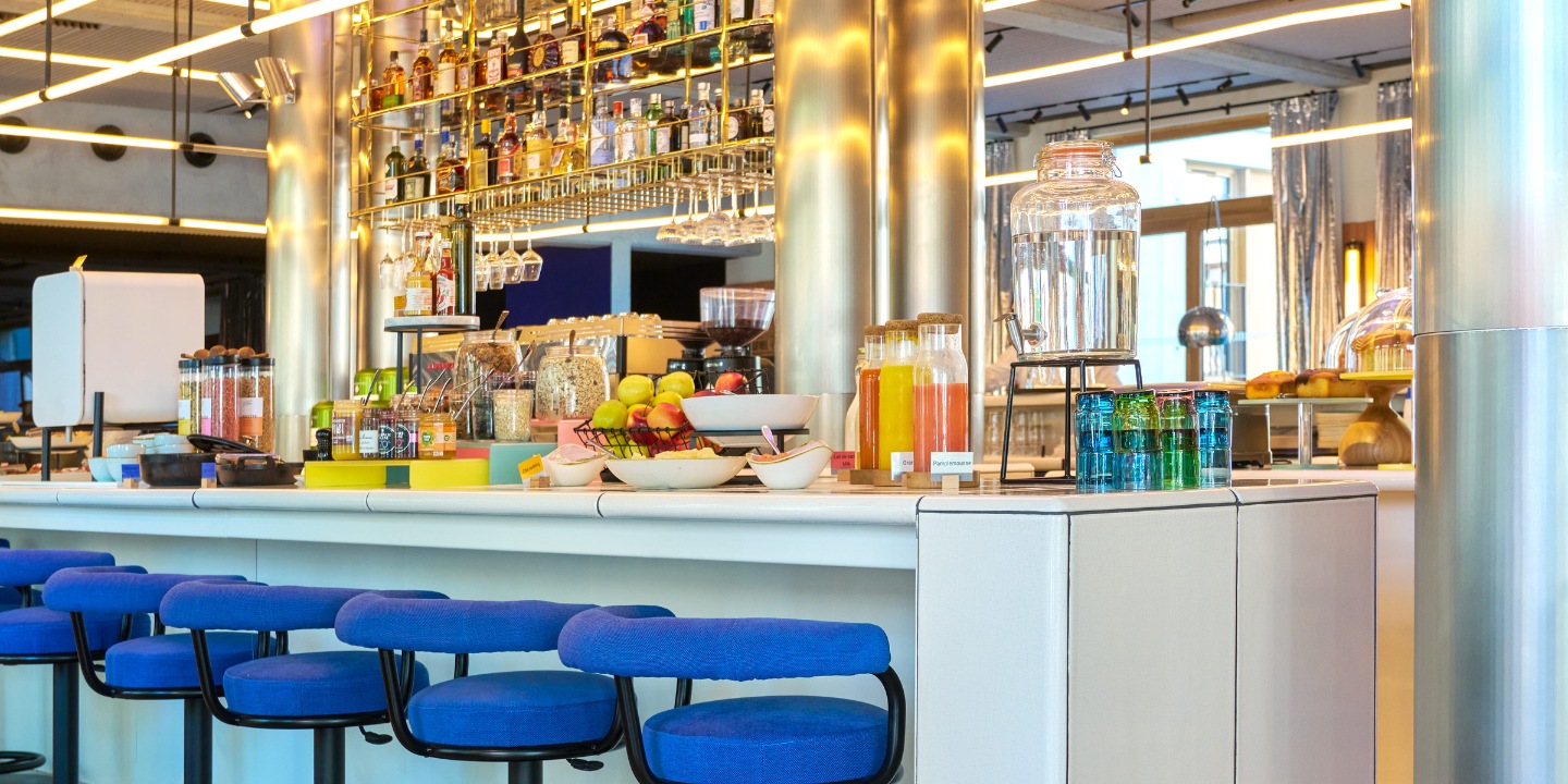 Breakfast buffet with fruit and juices at a bar with blue stools.