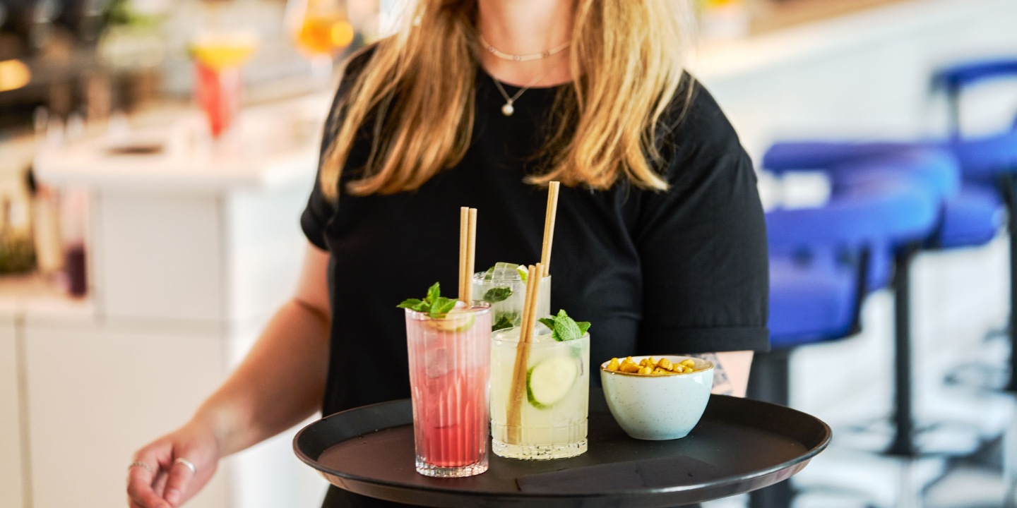 A server bringing cocktails and a bowl of snacks on a tray.