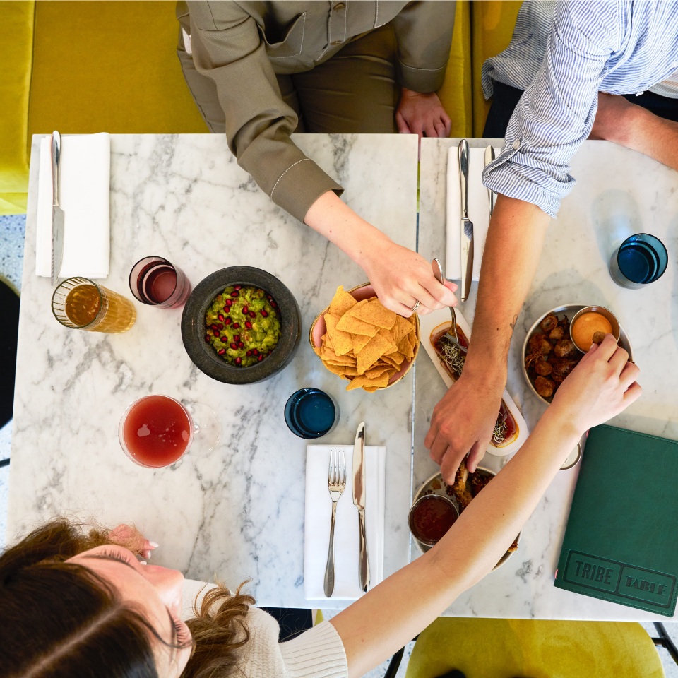 Friends sharing nachos, guacamole and drinks around a table.