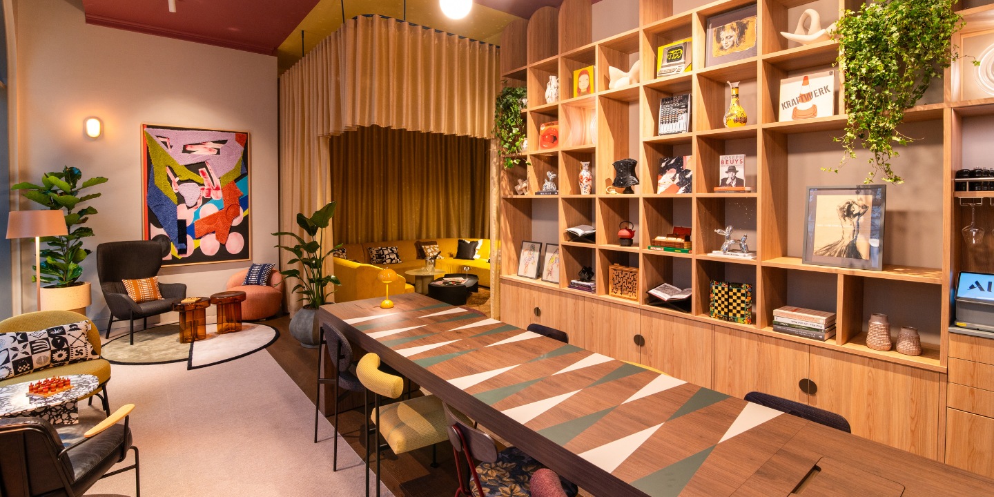 Stylish lounge with colorful seating, a modern art piece, greenery, and a sleek dining table, creating a cozy atmosphere.