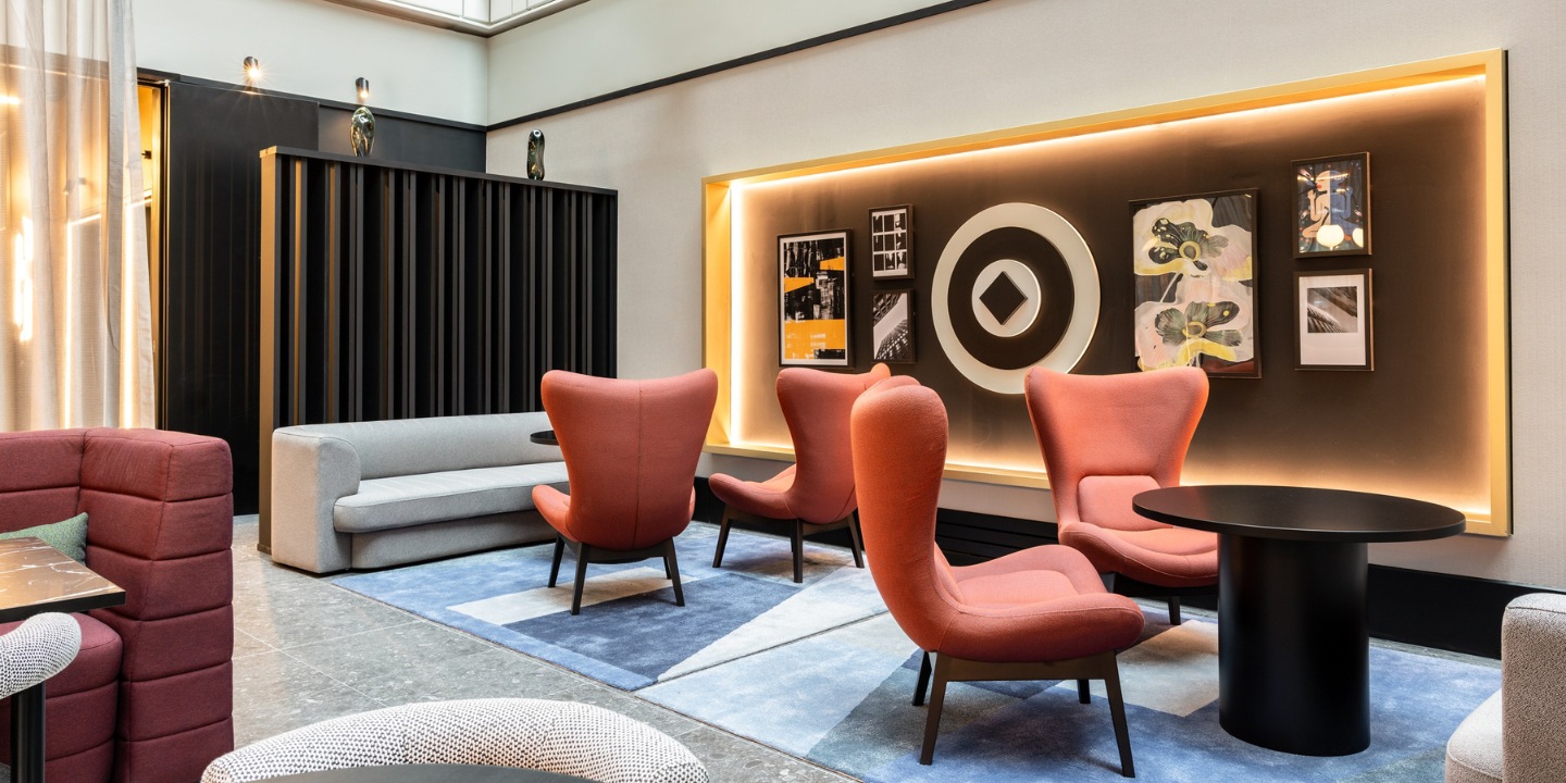 Modern lounge with orange chairs, a gray sofa, and artwork against a softly lit wall, creating a cozy ambiance.