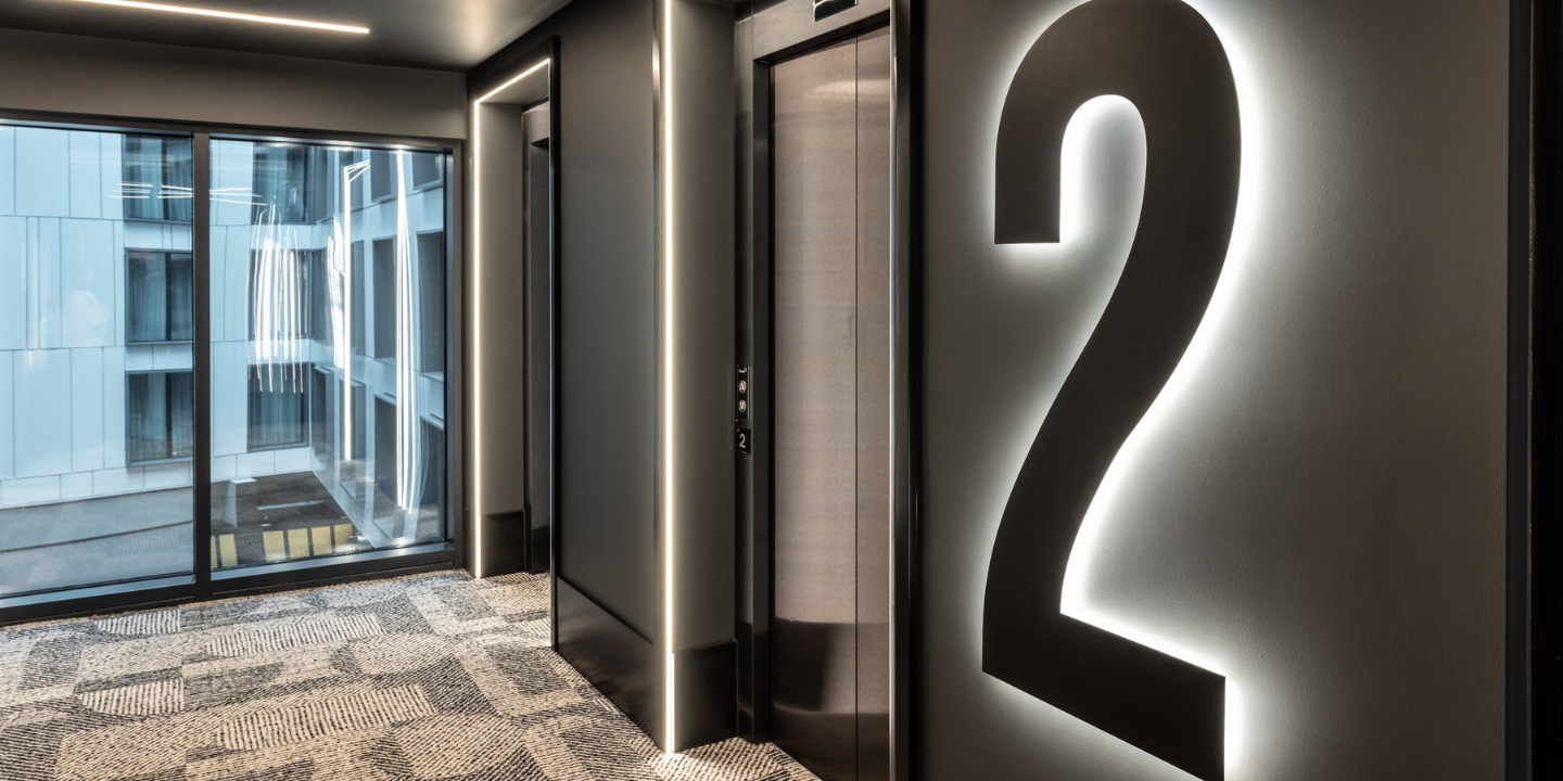 Modern elevator lobby featuring a large illuminated number 2, sleek design, and large windows with an urban view.