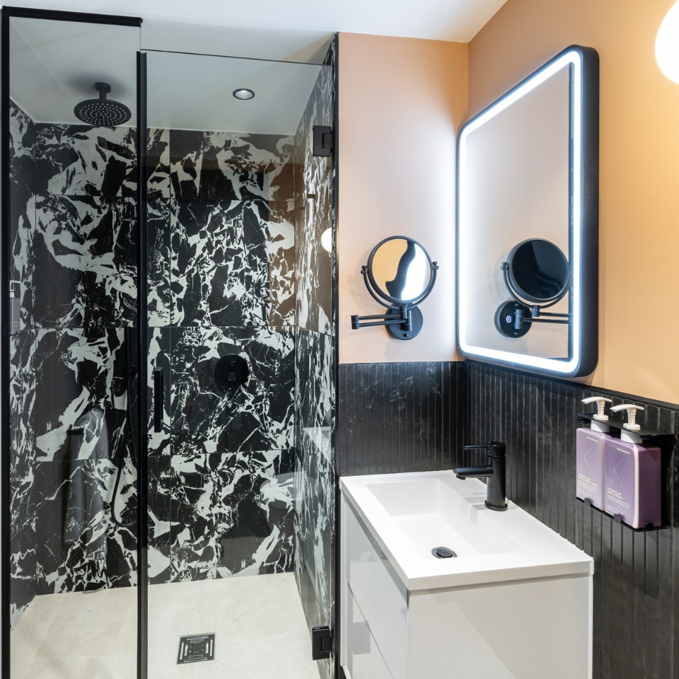Bathroom featuring a glass shower with black and white marble, sleek vanity, and illuminated mirror.