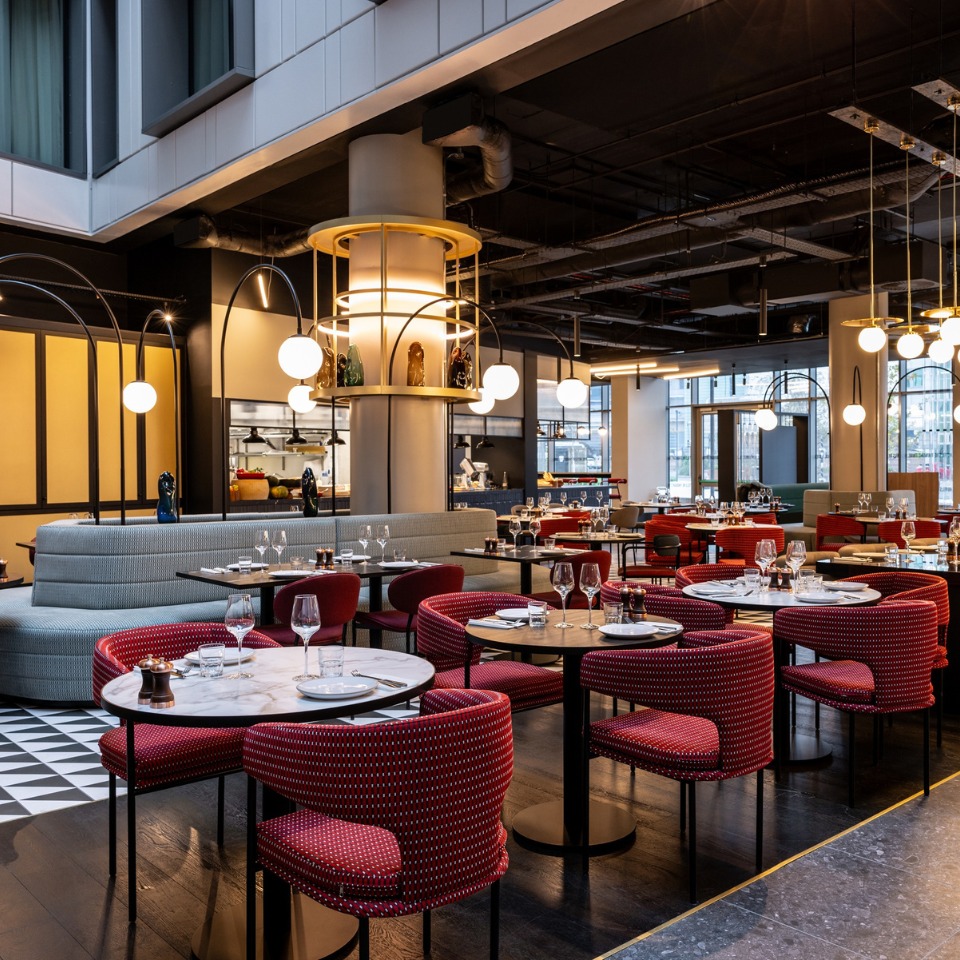 Restaurant with modern decor, featuring round tables, glassware, and a cozy ambiance enhanced by soft lighting and elegant textiles.