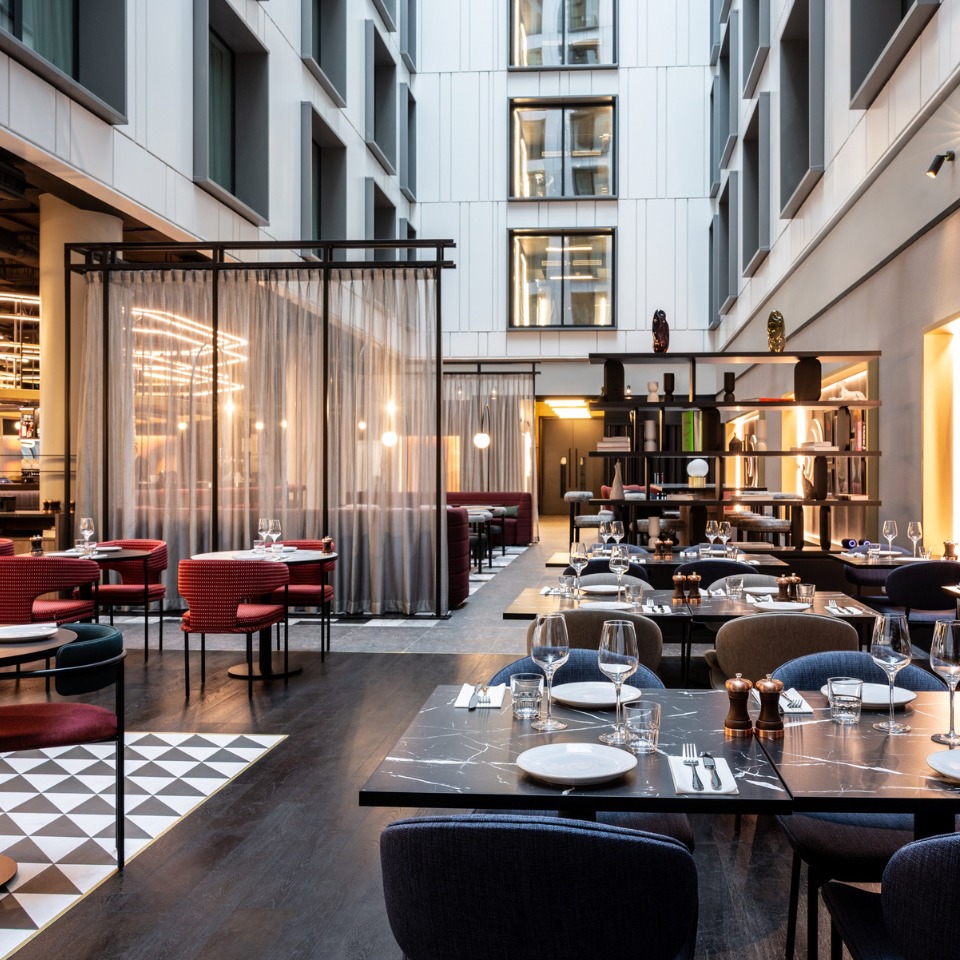 Restaurant with modern decor, featuring round tables, glassware, and a cozy ambiance enhanced by soft lighting and elegant textiles.
