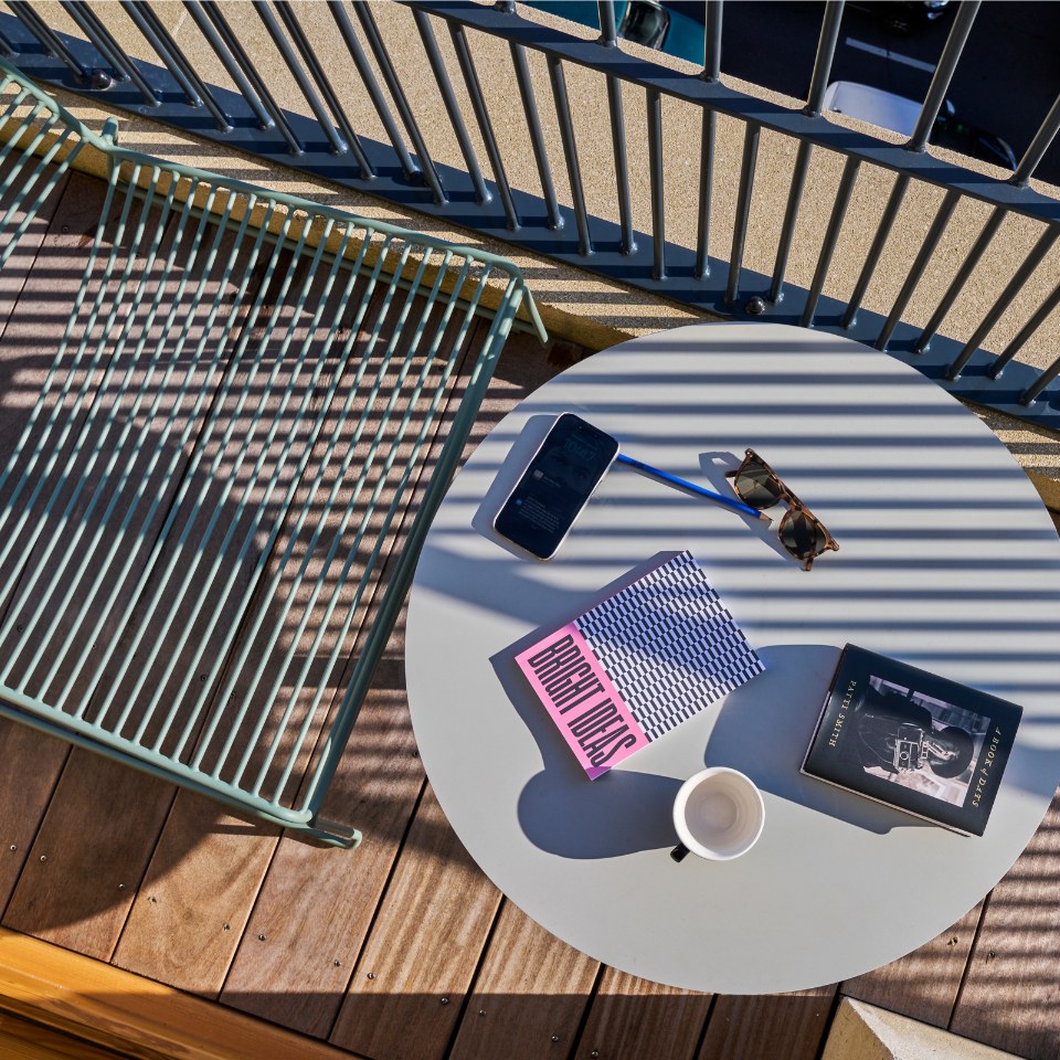 Table de balcon avec tasse de café, livres, lunettes de soleil et téléphone.