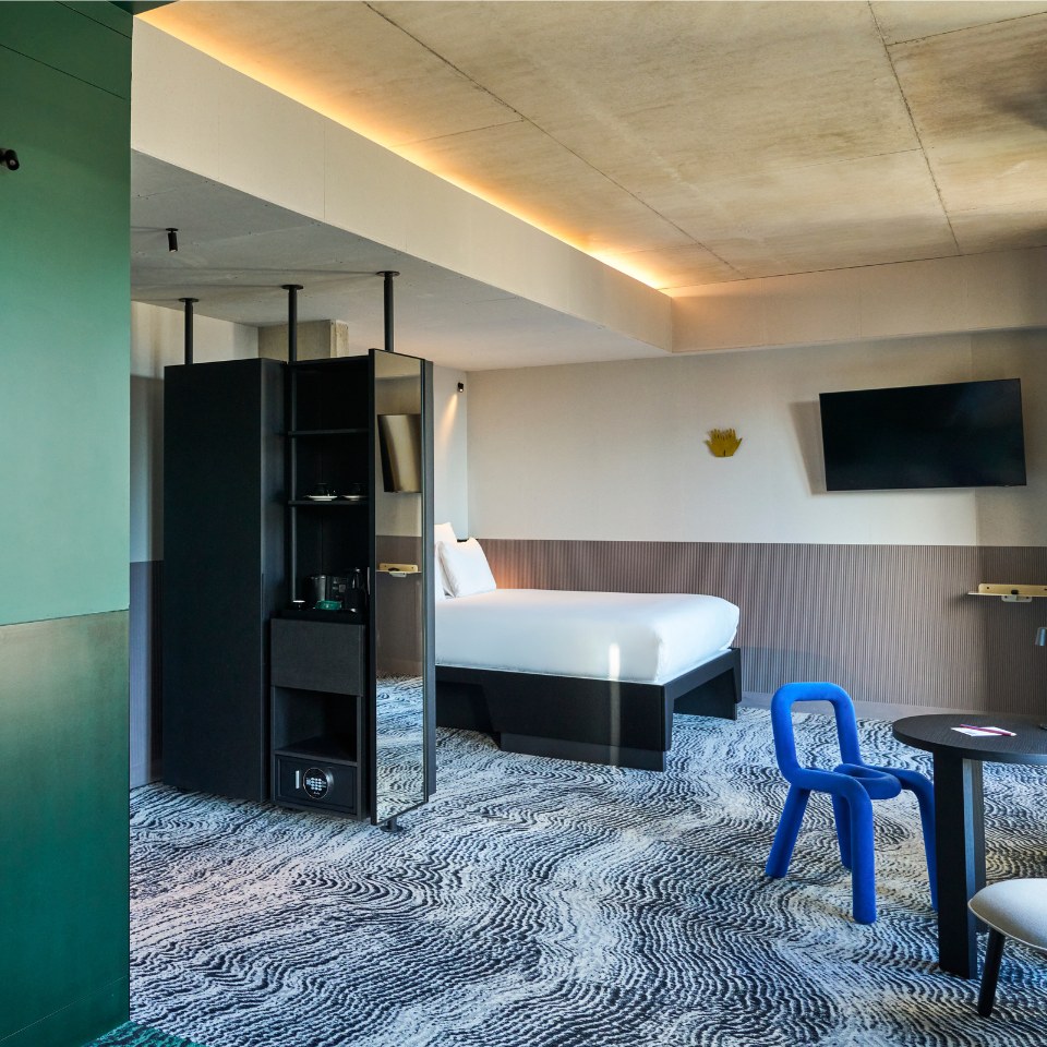 Chambre avec un lit, un fauteuil bleu et une télévision.