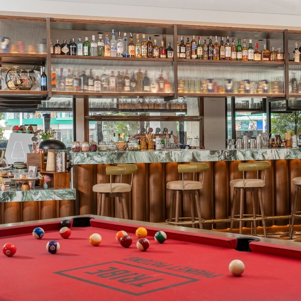 A stylish bar with a marble counter, high stools, and a well-stocked liquor shelf. A pool table with colorful balls is in the foreground.