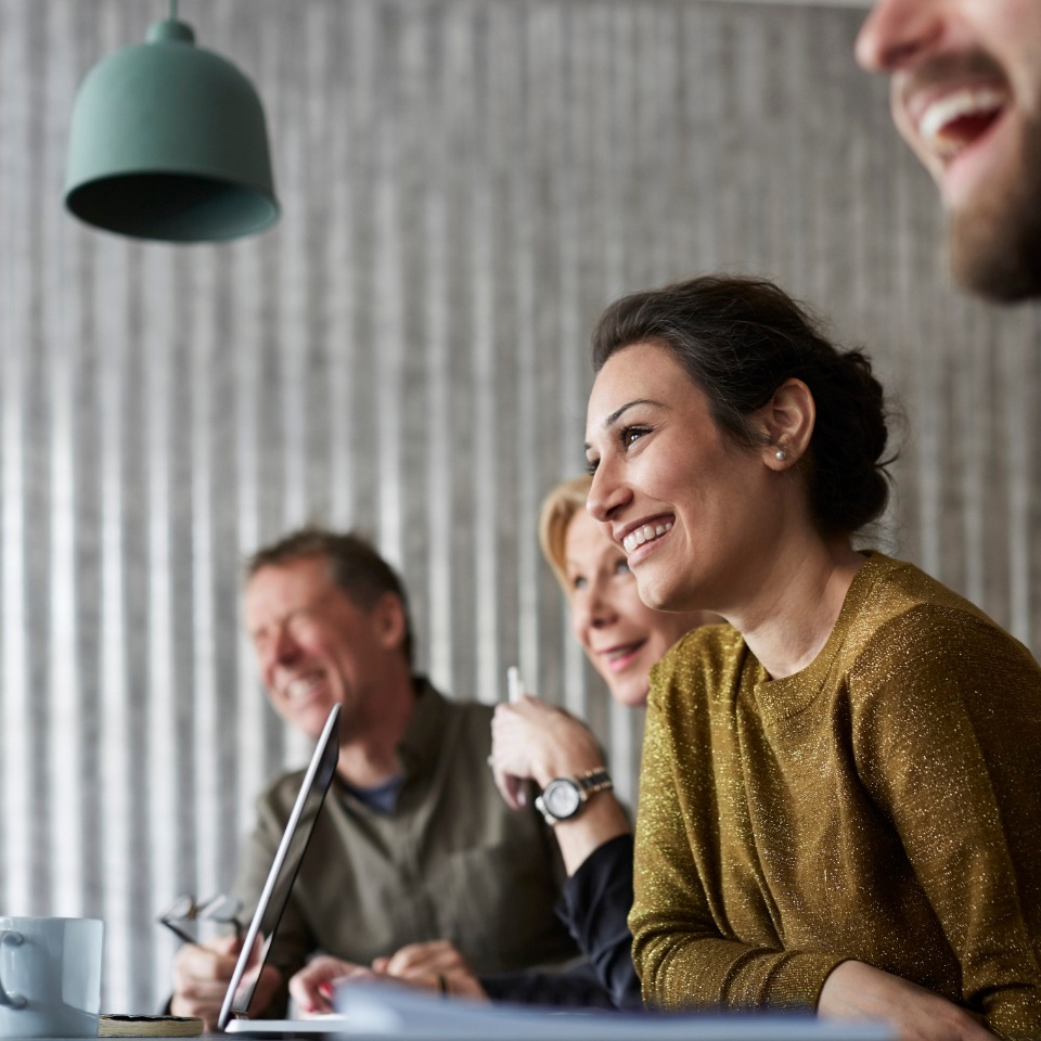 A group of people engaging in a discussion around a table, with warm lighting and a modern, industrial decor.