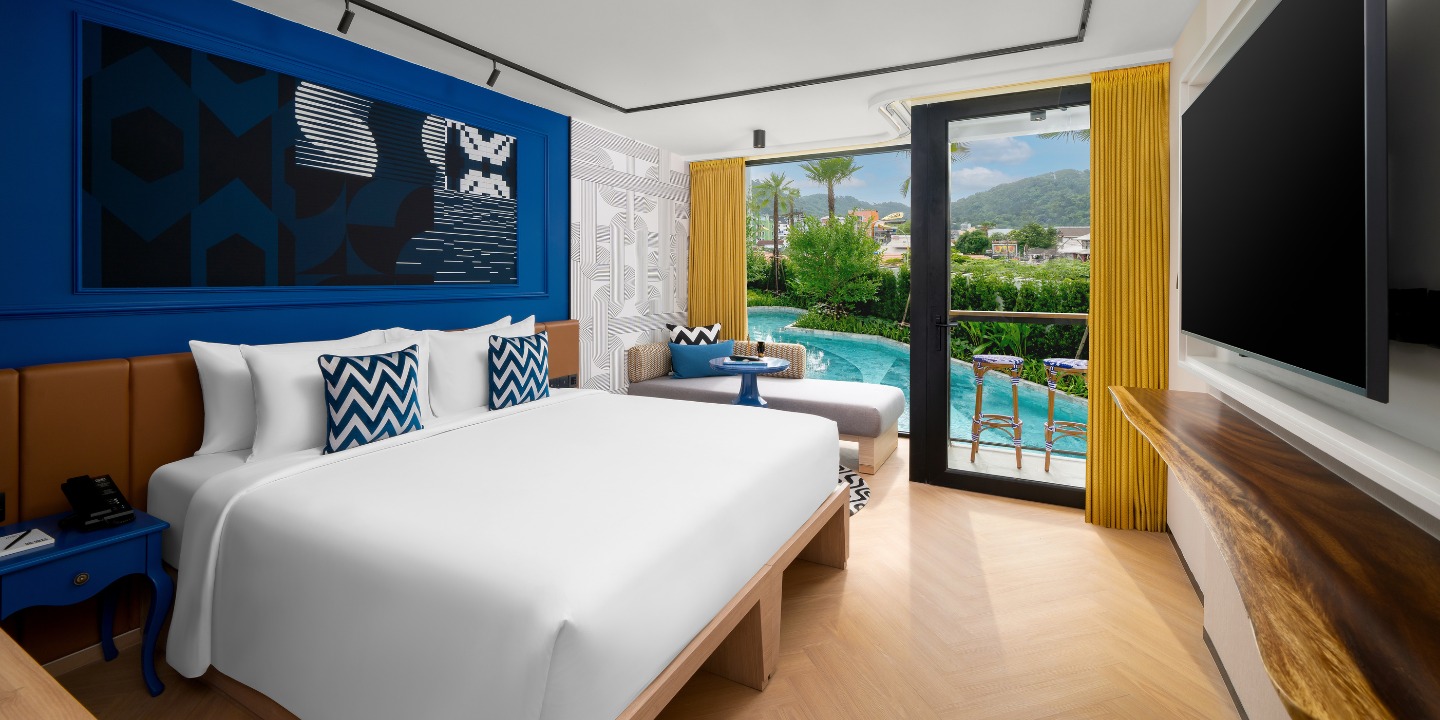 White double bed against a blue wall, with a balcony overlooking a pool.