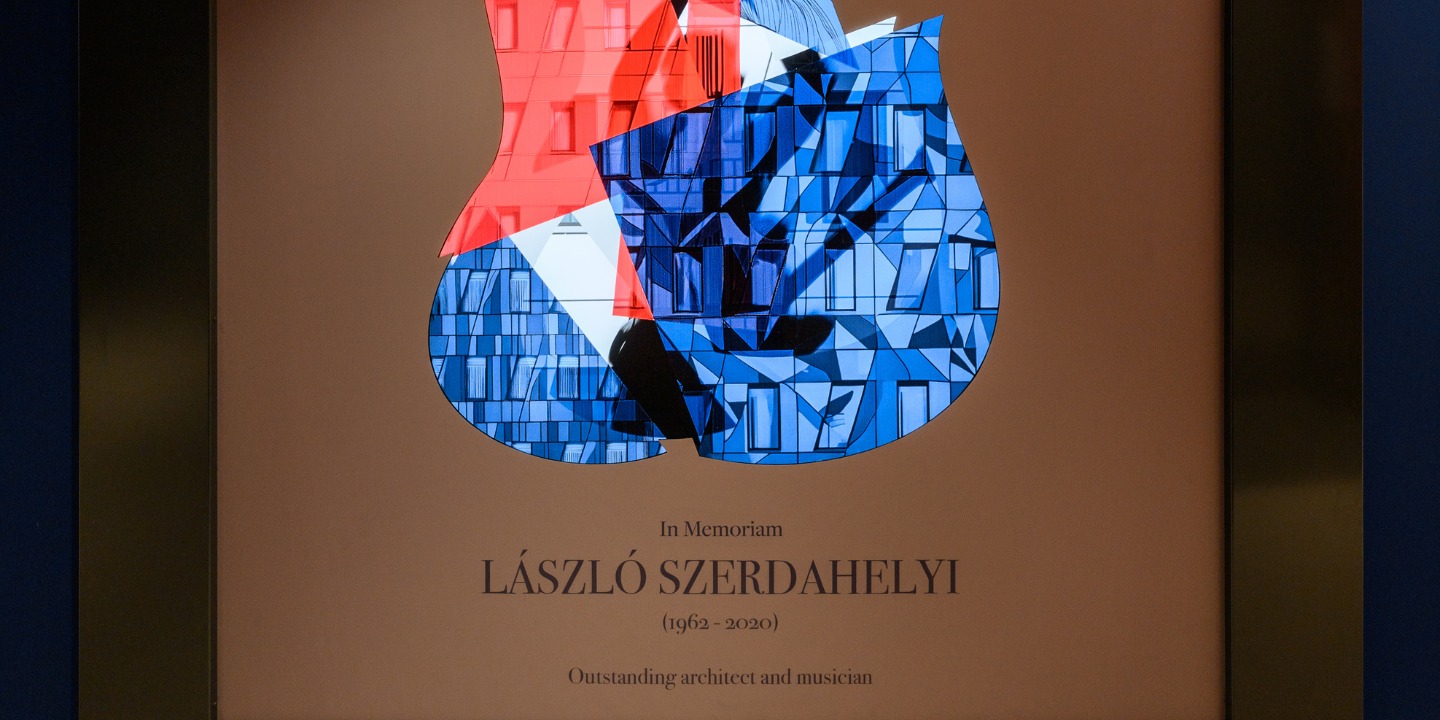 Illuminated artwork in the shape of an electric guitar, featuring red, blue, and white geometric patterns. The text below commemorates László Szerdahelyi.