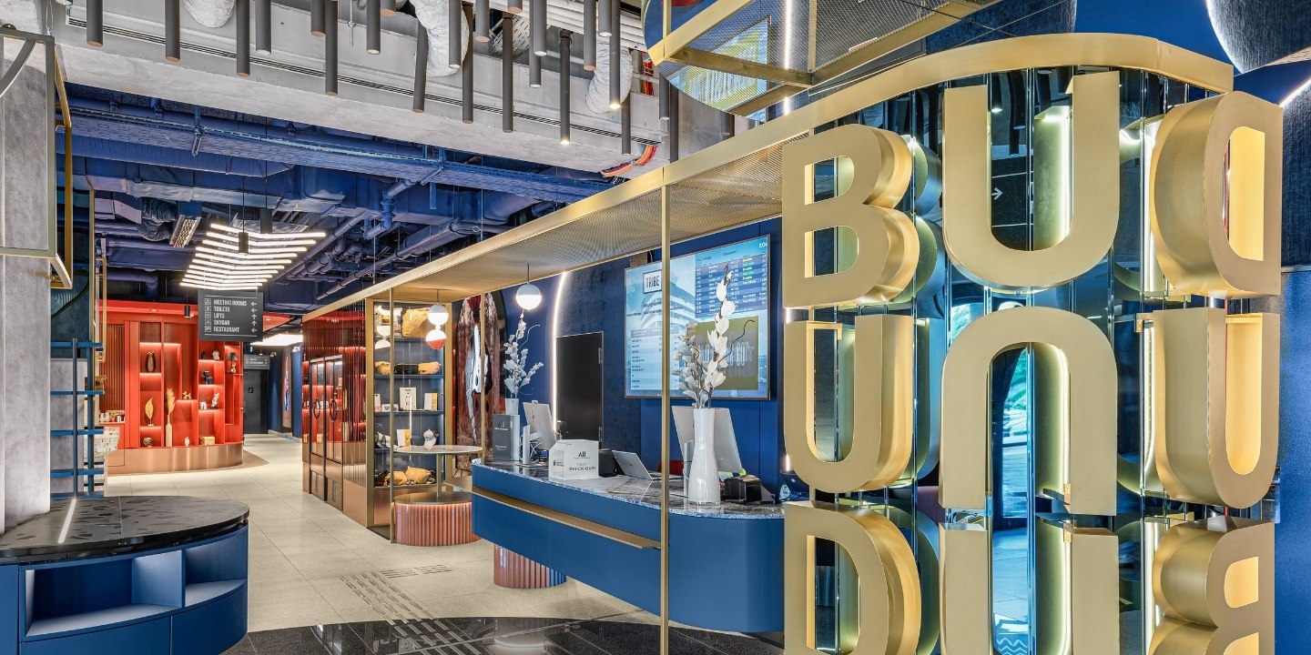 Modern reception area with vibrant blue and red decor, featuring unique displays and the "BUD" sign in bold gold letters.