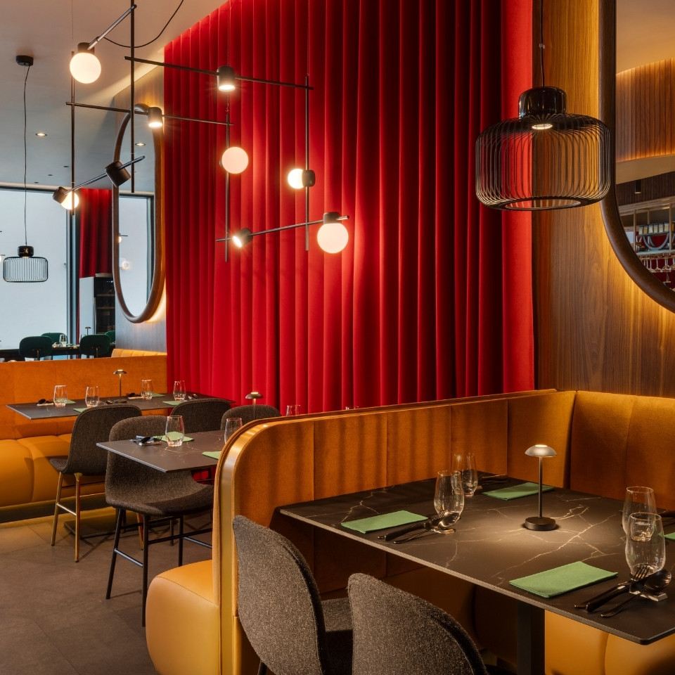 Intérieur de restaurant élégant avec des murs en velours rouge, un éclairage moderne et des assises moelleuses autour de tables joliment dressées.