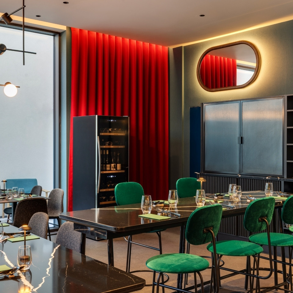Une salle à manger moderne avec des chaises en velours vert, une table noire épurée et un rideau rouge saisissant en toile de fond.