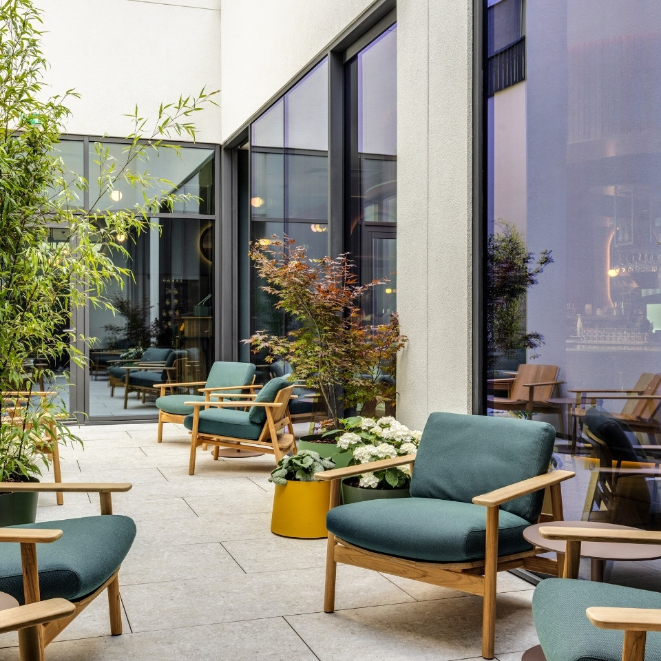 Un élégant espace lounge extérieur avec des chaises vertes modernes, des plantes en pot et de grandes baies vitrées reflétant un intérieur chaleureux.