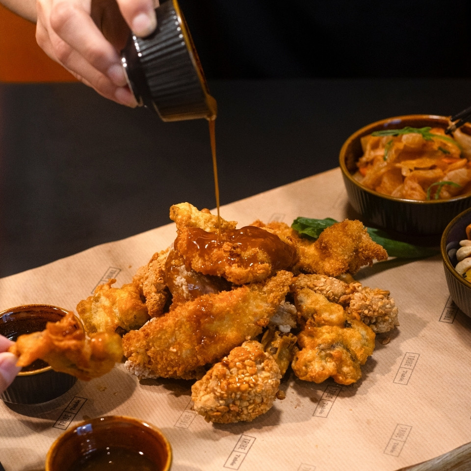 Une personne verse de la sauce sur du poulet frit et divers accompagnements sur une table.