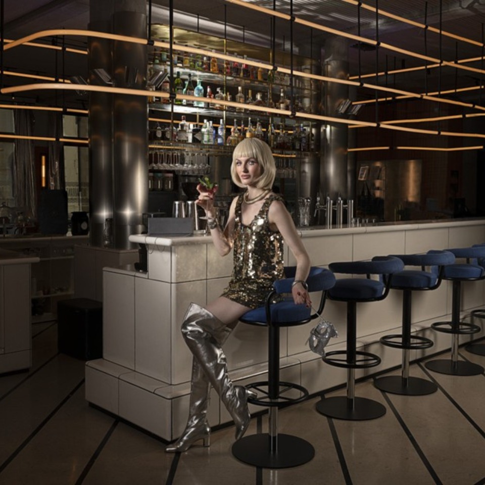 A woman in a shimmering outfit sits at a bar.