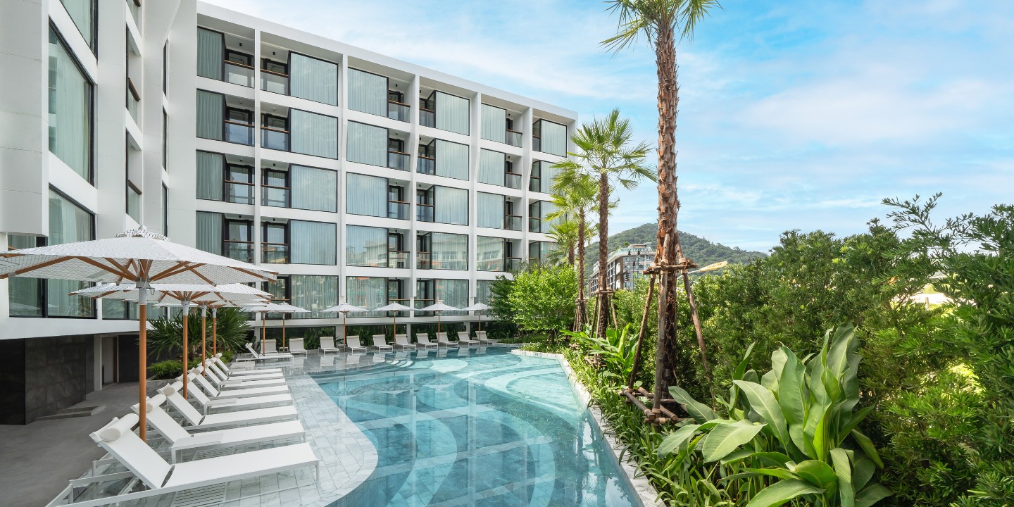 Outdoor swimming pool with loungers beside a modern hotel building.