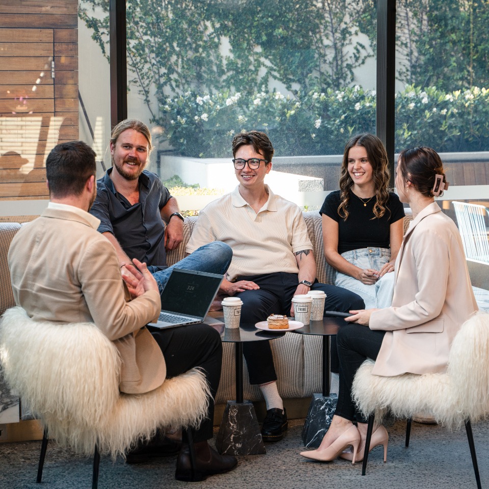 A group discusses a laptop around a lounge table.
