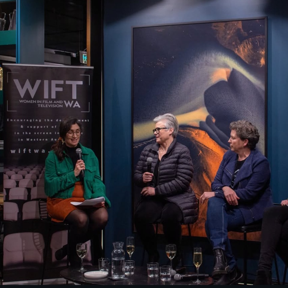 Panel discussion with three speakers seated in front of an artwork.