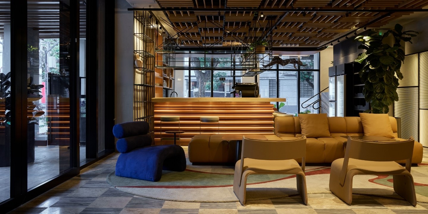 Modern lounge with warm lighting and contemporary furniture. Features a sleek wooden reception desk, cozy brown sofas, and large windows, creating an inviting atmosphere.