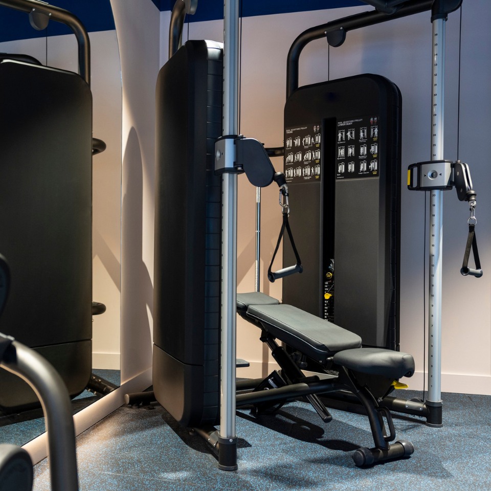 A sleek gym setup featuring a multifunctional weight machine and an adjustable bench, set against a modern interior.