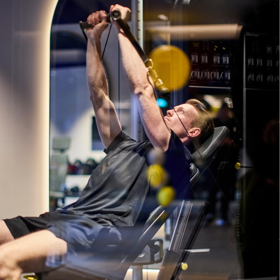 A person exercises on a gym machine, gripping the handles with arms extended, focusing on strength training in a modern fitness environment.