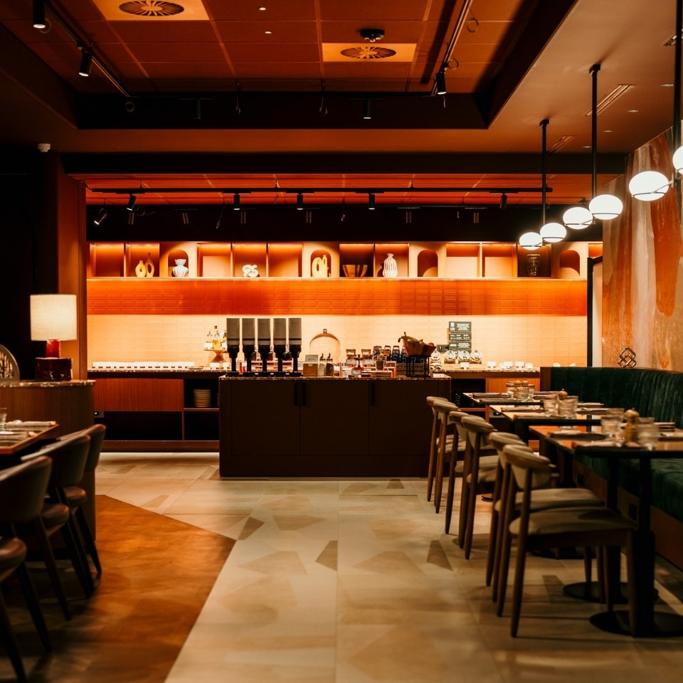 Modern restaurant interior featuring a warm-lit bar area, stylish seating, and decorative shelving in earthy tones.