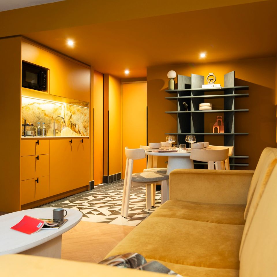 Stylish modern kitchen with warm orange walls, geometric tiles, and cozy seating. A round dining table is set for dinner, creating an inviting, cozy atmosphere.