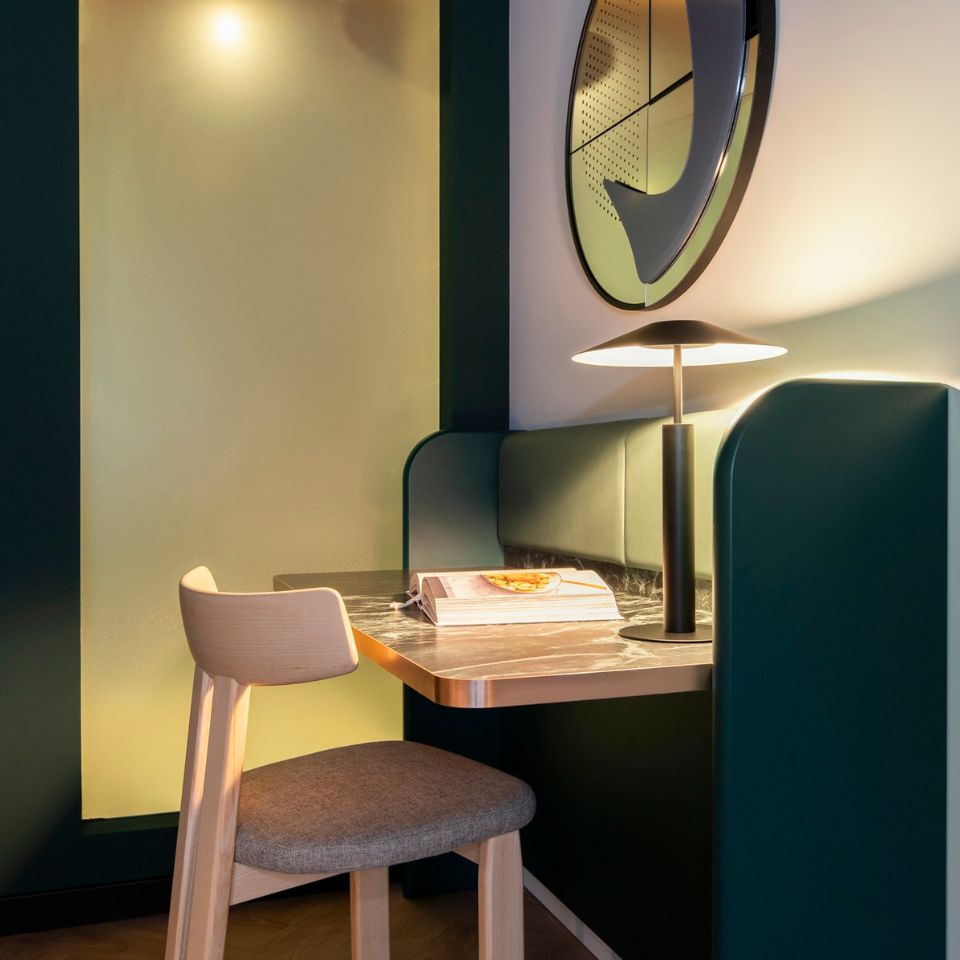 A cozy nook with a wooden chair and a dark marble table, featuring a glowing lamp and an open book. Mood is warm and inviting, with soft lighting.