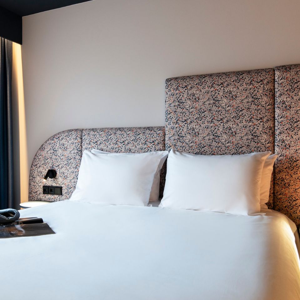 A neatly made bed with a white comforter and two pillows, set against a speckled, textured headboard. Soft lighting creates a calm, inviting ambiance.