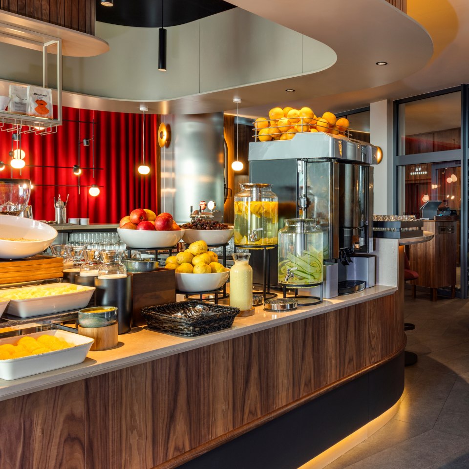 Elegant buffet with fresh fruits like apples, lemons, and oranges, alongside juice dispensers in a vibrant, warmly lit restaurant setting.