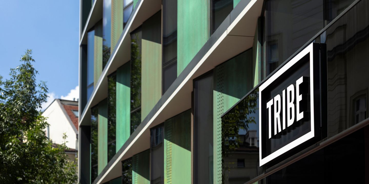 The image shows a modern building facade with green accents, featuring a prominent black and white sign reading "TRIBE."
