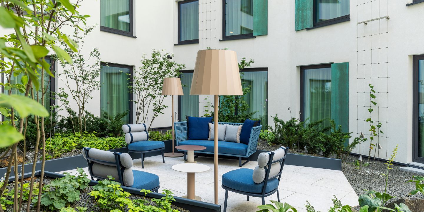A stylish courtyard with modern blue furniture, two lamps, and greenery, creating a tranquil outdoor seating area.