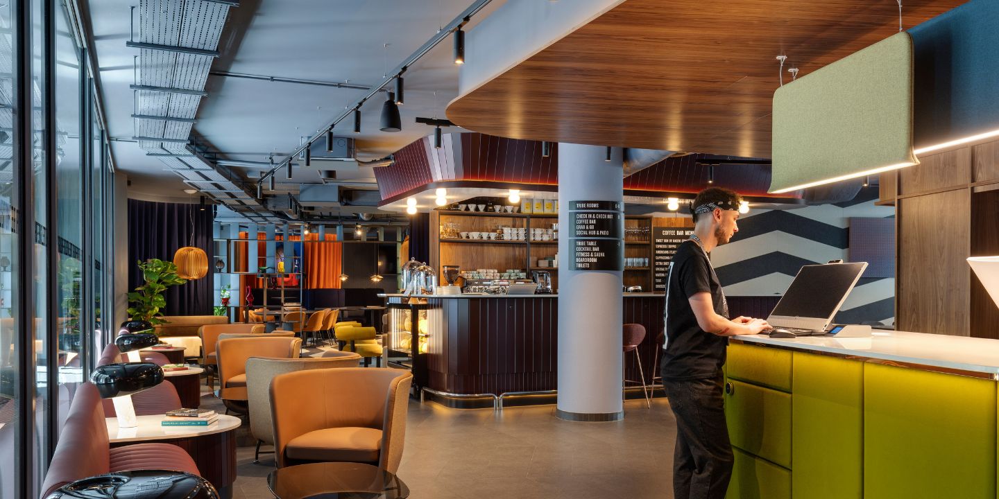 Modern café interior featuring colorful seating, a sleek counter, and a barista working on a laptop amidst stylish decor.