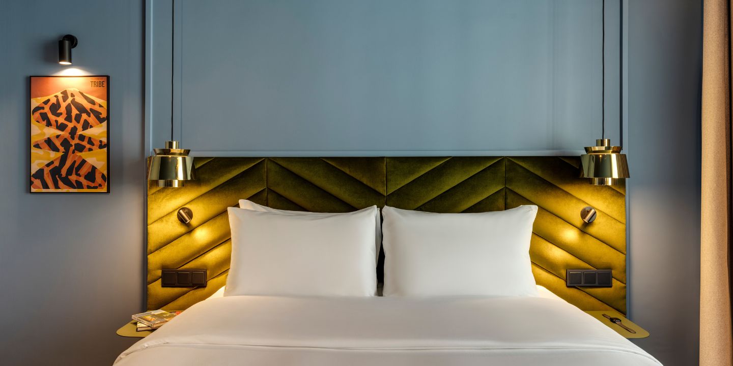 Stylish hotel room with a green chevron headboard, white pillows, modern lighting, and a colorful framed artwork on the wall.
