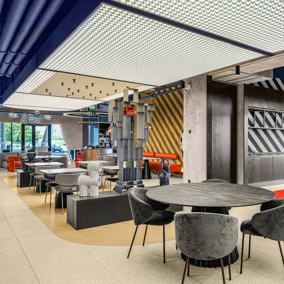 Modern, stylish lounge with unique art sculptures, round marble table, plush chairs, and geometric ceiling lighting in a bright, open space.