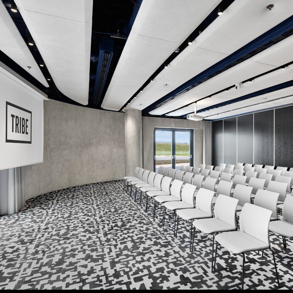 Rows of white chairs facing a TRIBE screen.