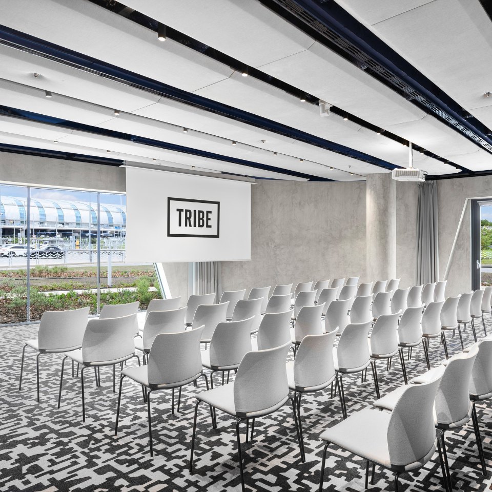 Rows of white chairs facing a TRIBE screen.